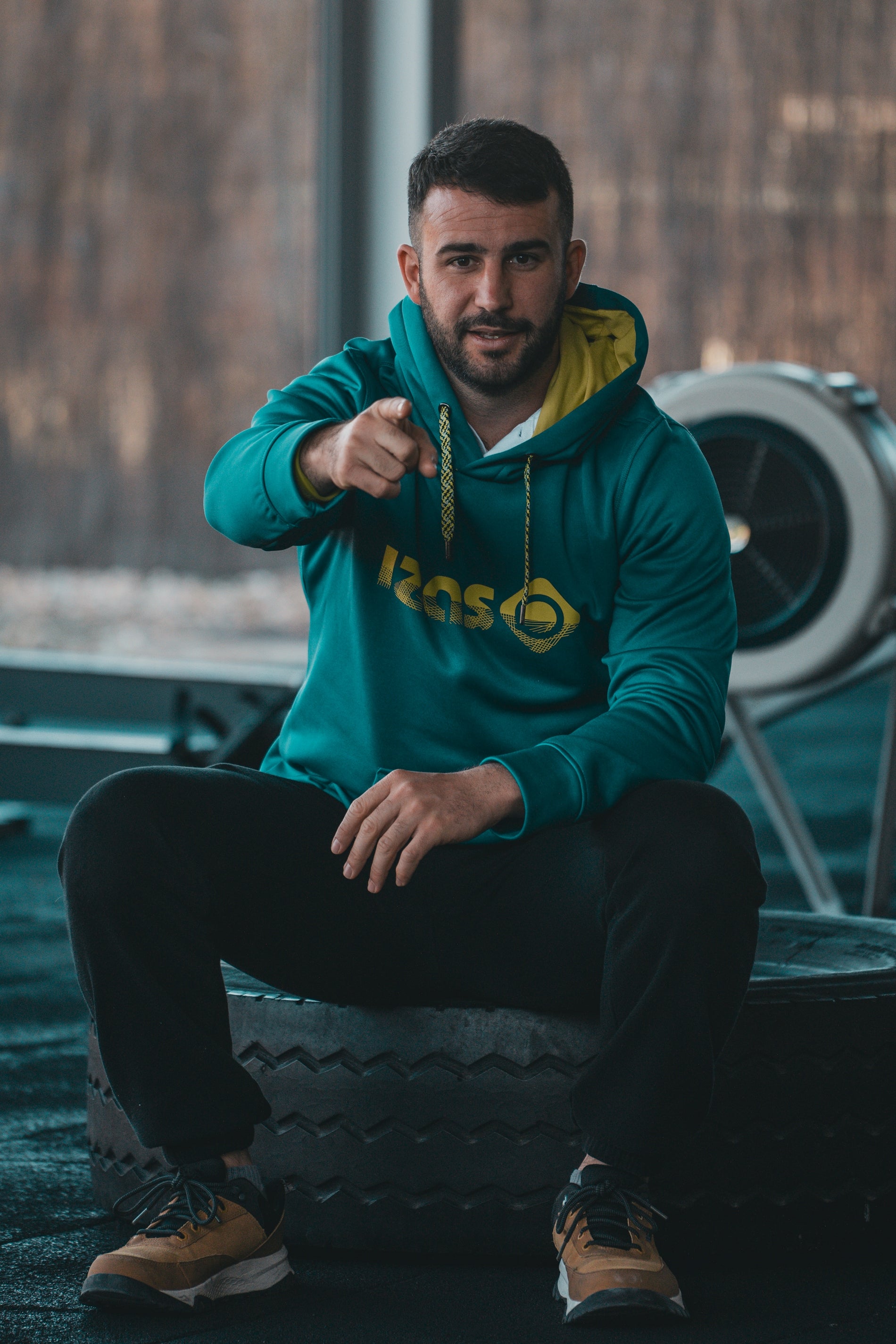 A man in a green hoodie sitting on a tire